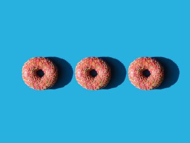 three pink doughnuts that are lined up on a light blue background to look like an ellipsis