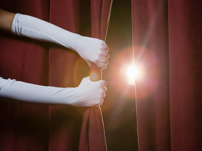hands pulling back a theater curtain