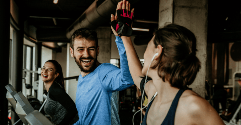 a man and two women in the gym, the man is high fiving one of the women as they all use the exercise equipment