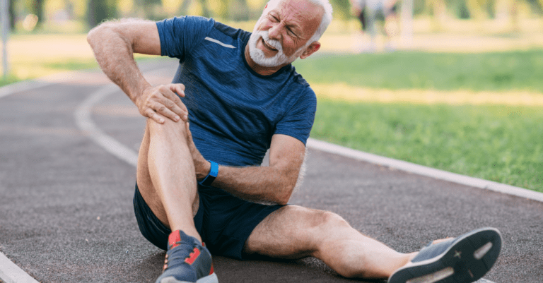 an older gentleman sitting on a track holding his knee in pain