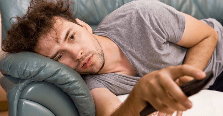 a man laying on a couch using a remote