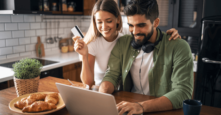 a couple smiling in front of a computer, the woman holds up a credit card