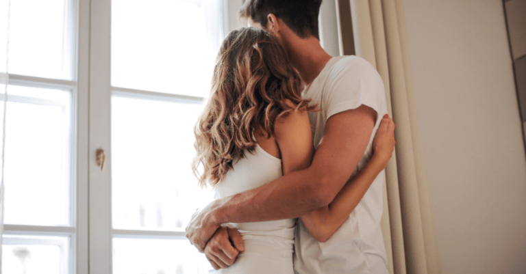 a couple holding each other in front of a window