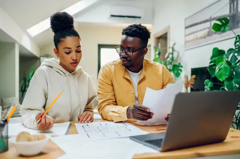 Multiracial couple looking into the blueprints of their future home and making a financial plan for that investment. Romantic diverse couple working together at home.