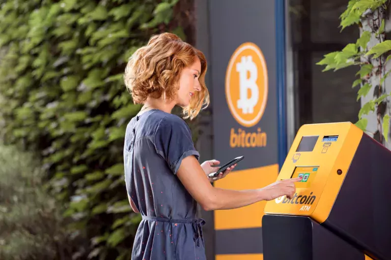 Woman in front of ATM with Bitcoin sign next to it