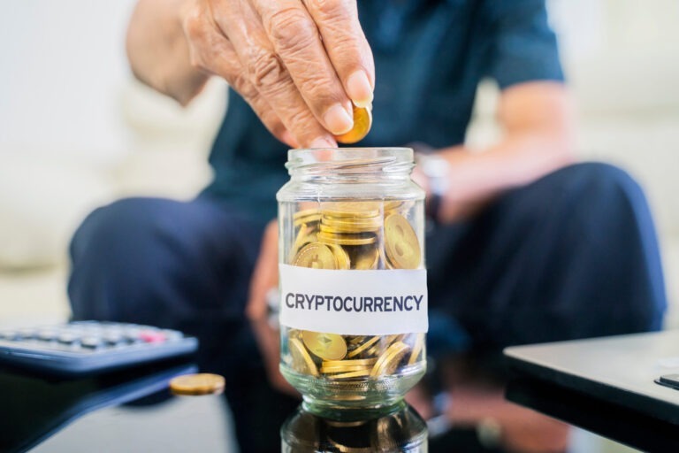 Hand putting gold coins in a jar labeled 'cryptocurrency'