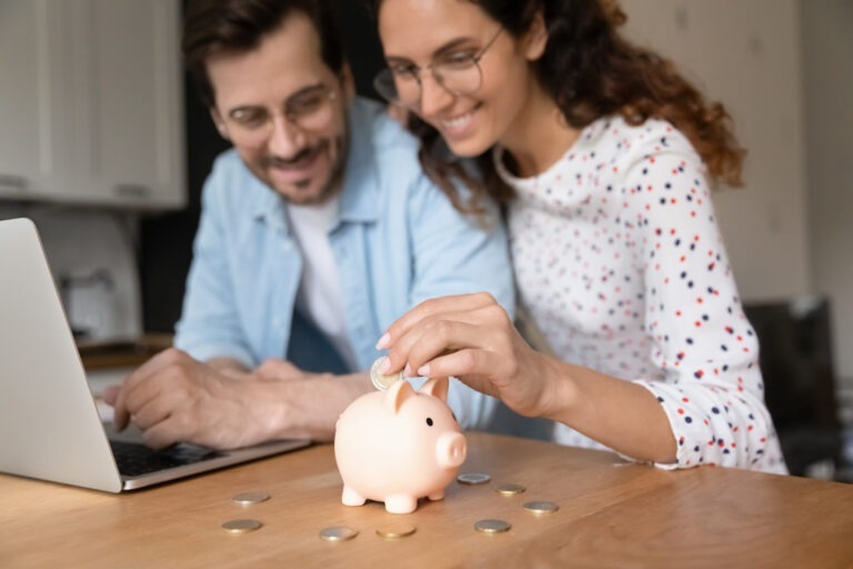 Man and woman put coins in a piggy bank in their kitchen