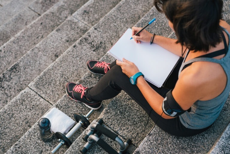 Person sitting next to dumbbells and writing notes