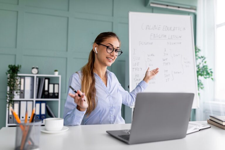 Woman in button up shirt and glasses in an office, in front of a white board with words on it.