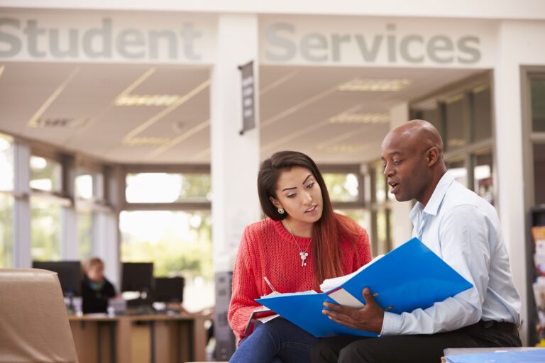 Two people looking at a folder under a sign that says student services
