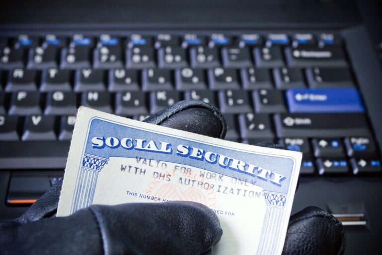 Computer keyboard with a gloved hand holding a social security card