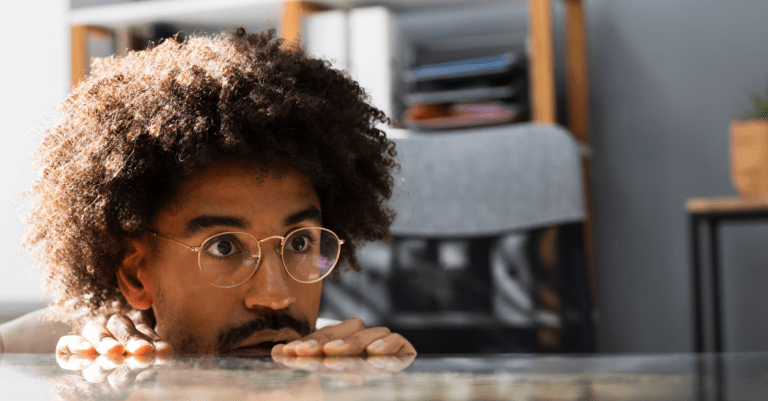 a man hiding behind a desk looking apprehensive