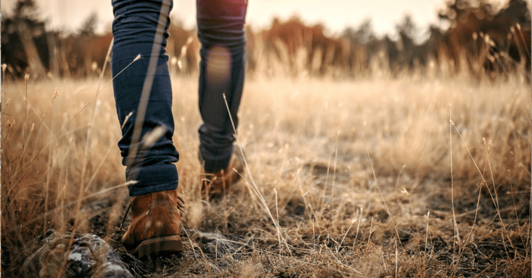 Feet in leather shoes walking in a dry grassy field.