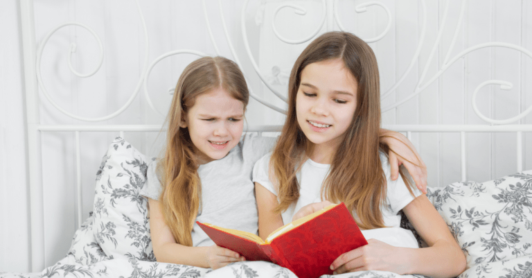 two young girls reading a red book together on a bed