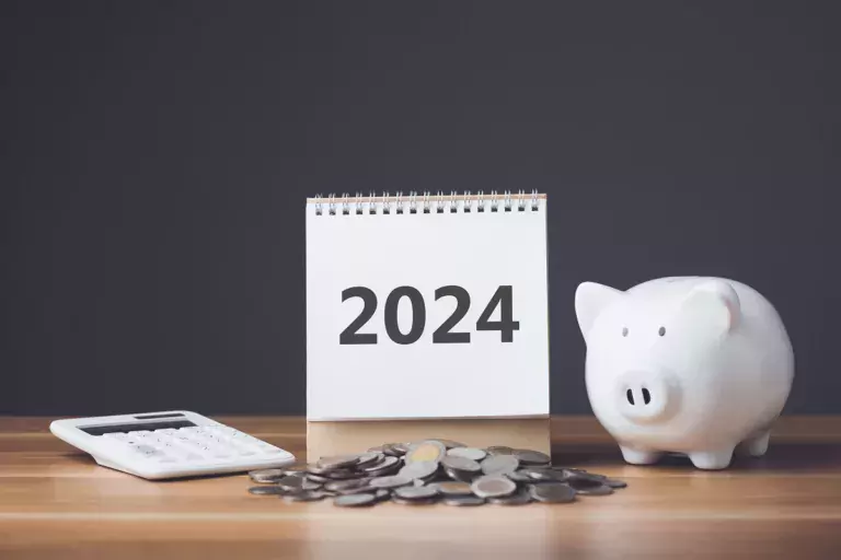 A calculator, calendar that says "2024." and a piggy bank depicting saving for retirement in 2024.