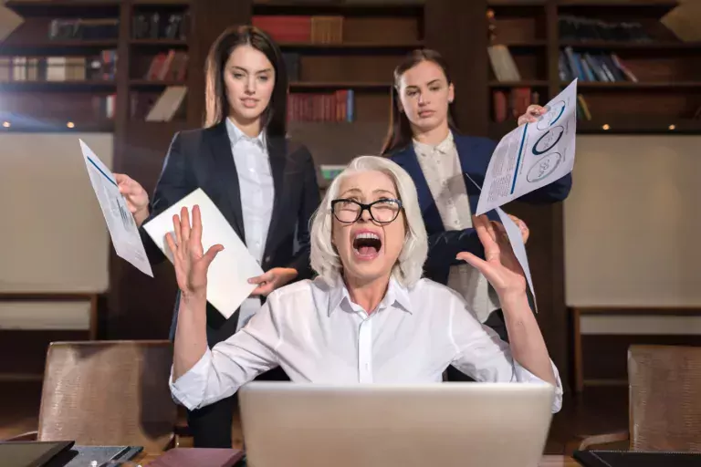 A female boss with hands up and mouth open wide, and two coworkers. Showing burnout at work.