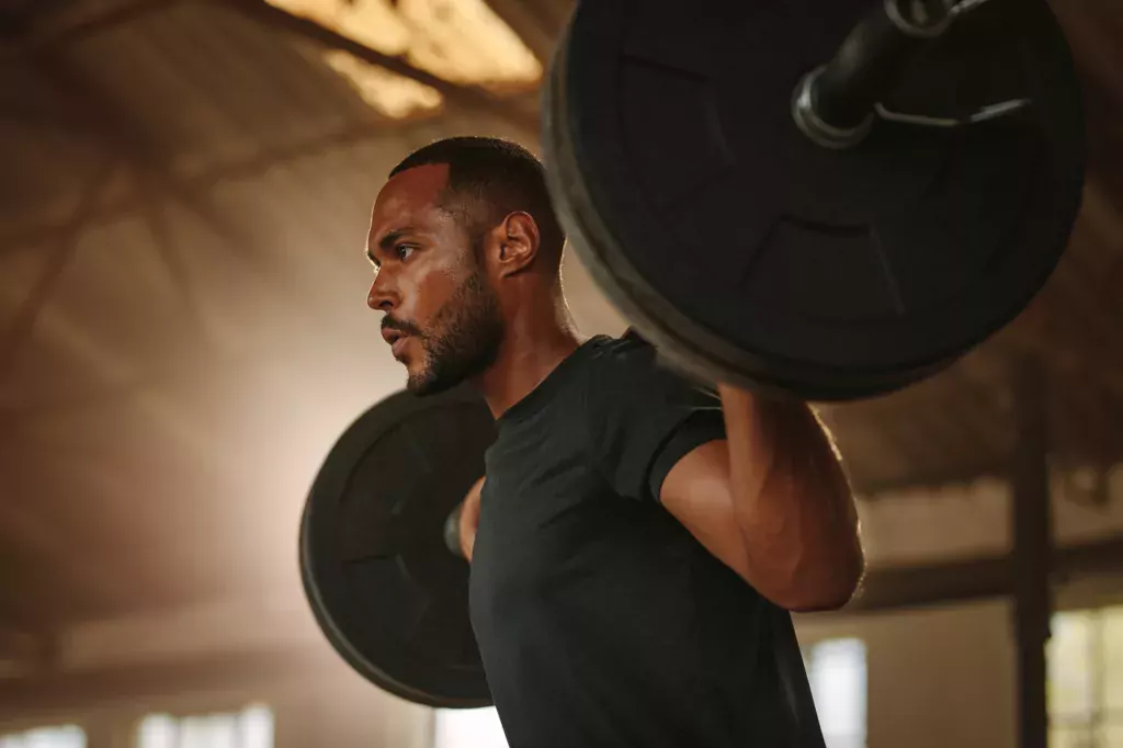 Man exercising with barbell. Male bodybuilder doing weight lifting workout at gym.