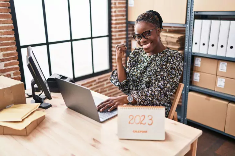 Woman at her desk pumping her fist in celebration, and a 2023 calendar on her desk