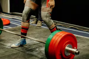 Person standing behind weighted barbell. Person has sleeves on their knees. 