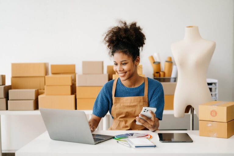 Woman in an apron with boxes behind her and with a laptop and calculator