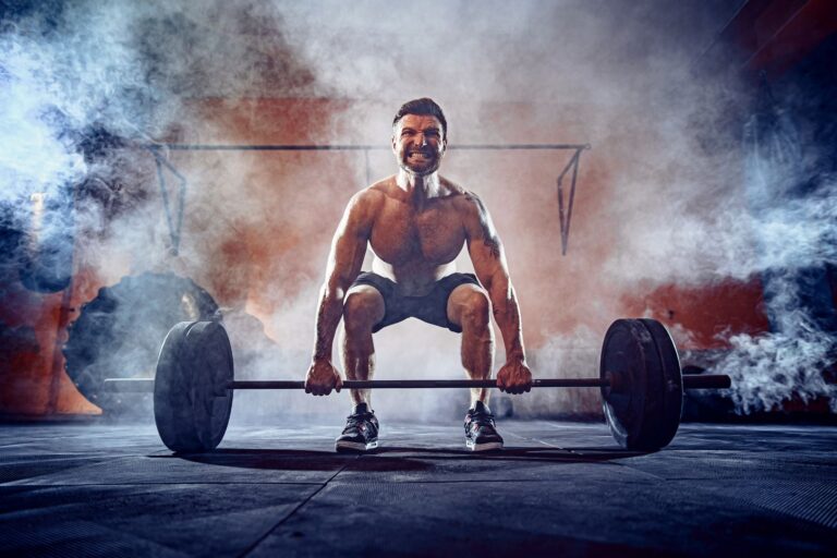 Man with muscles squatting at a barbell with smoke rising behind him